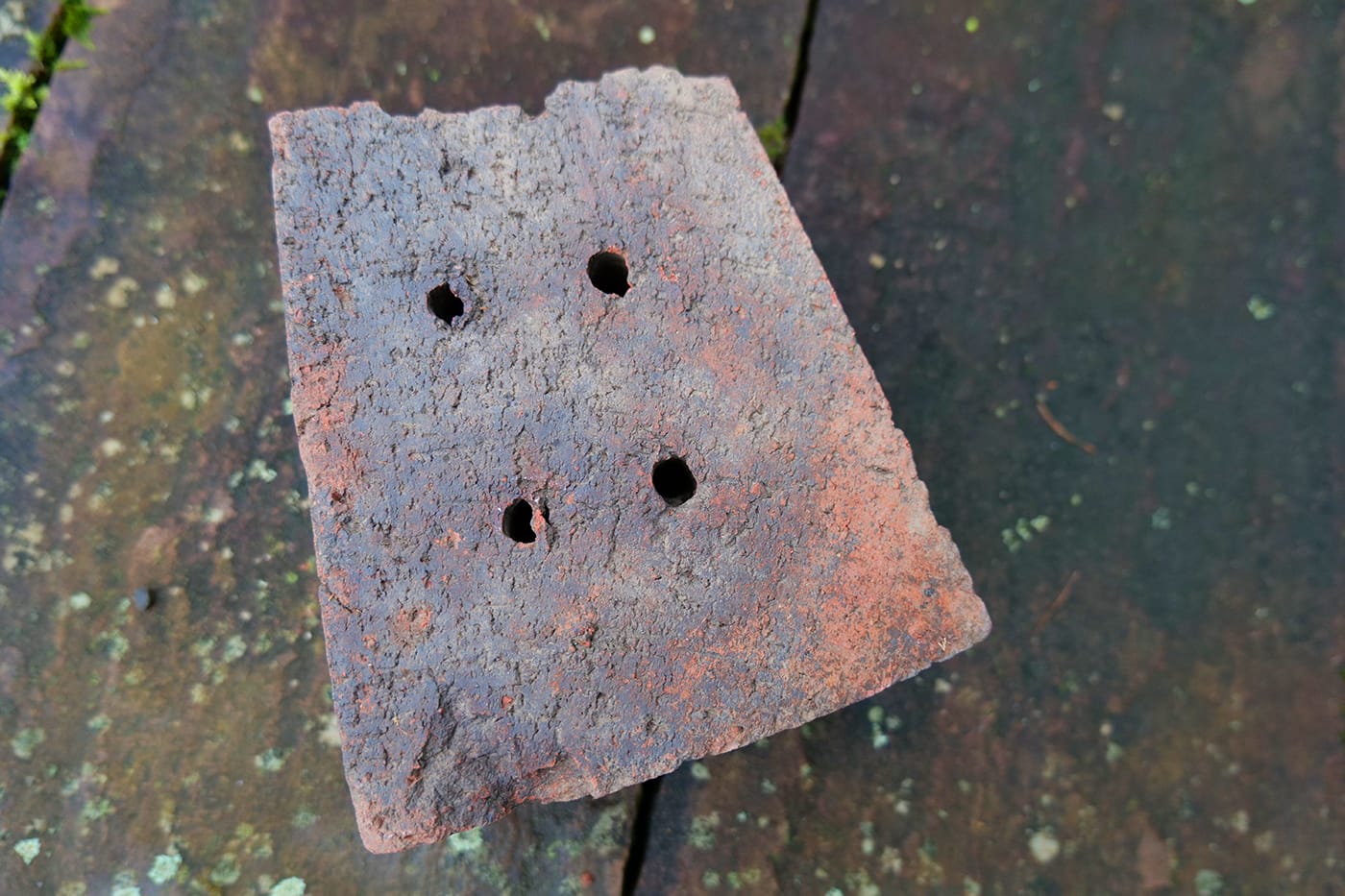 Trapezförmiger Lehmziegel, breitseits mit drei Lochpaaren gelocht (vermutlich Brunnenziegel).